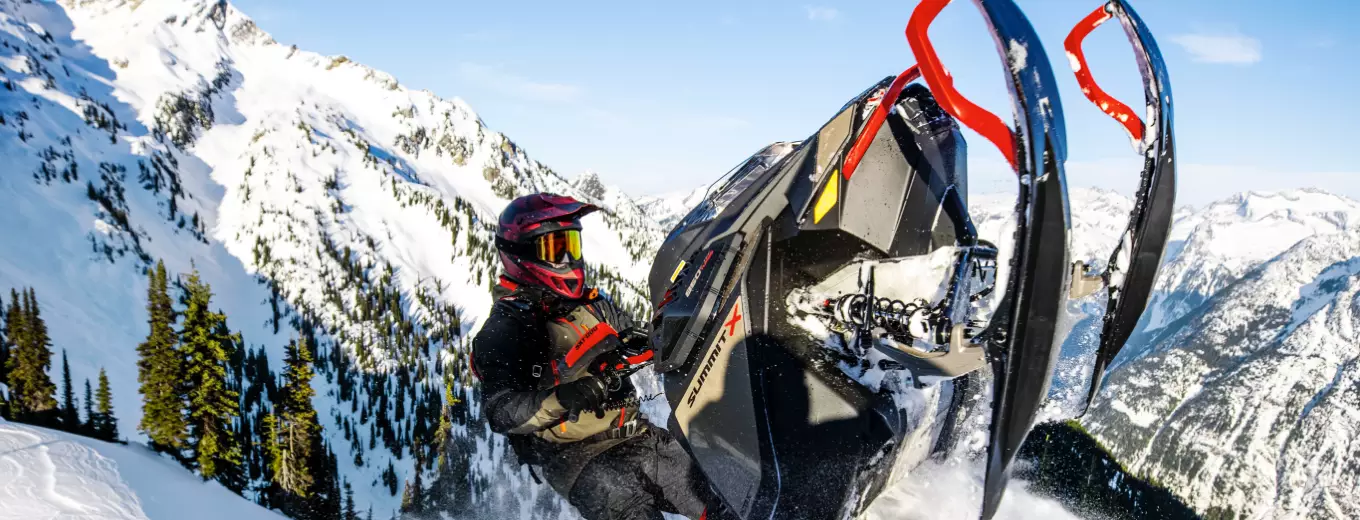 Person på snöskoter av märket Ski-Doo i snötäckt bergslandskap.