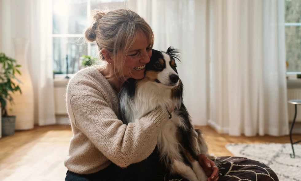 Kvinna sitter på golvet och kramar en hund.