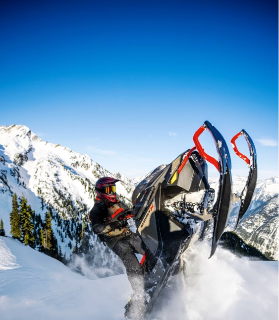 Person på snöskoter av märket Ski-Doo i snötäckt bergslandskap.