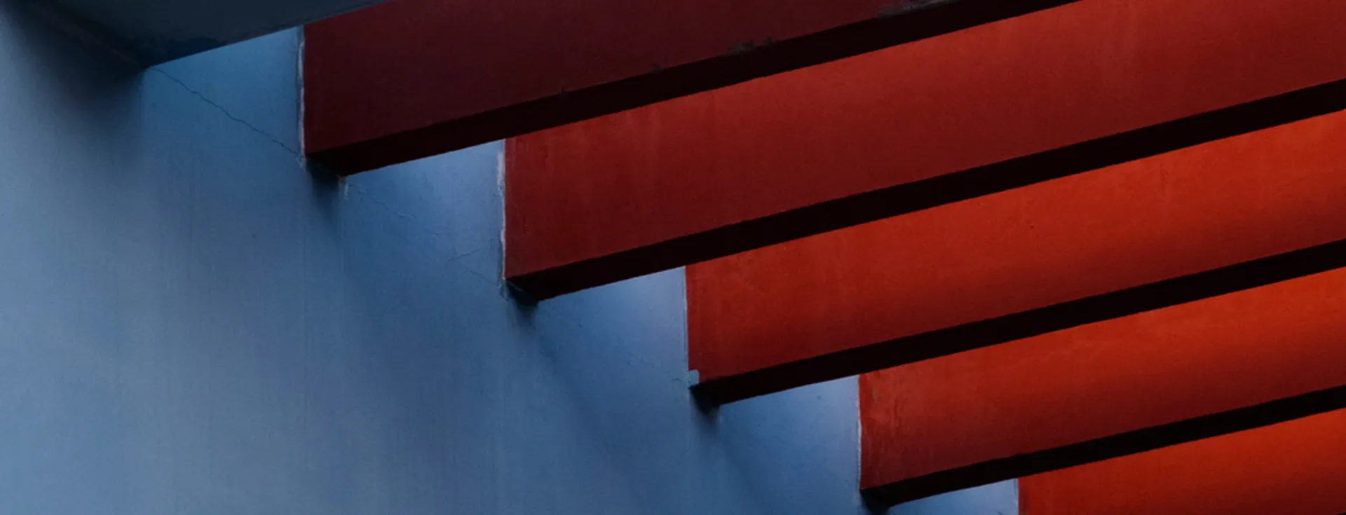 En abstrakt bild av röda trappsteg mot en blå vägg. Kontrasten mellan de två färgerna skapar ett iögonfallande mönster