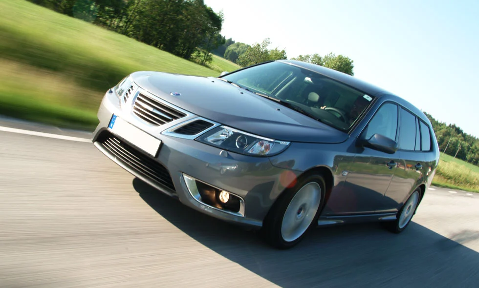 En grå Saab 9-3 SportCombi kör snabbt på en sommarväg