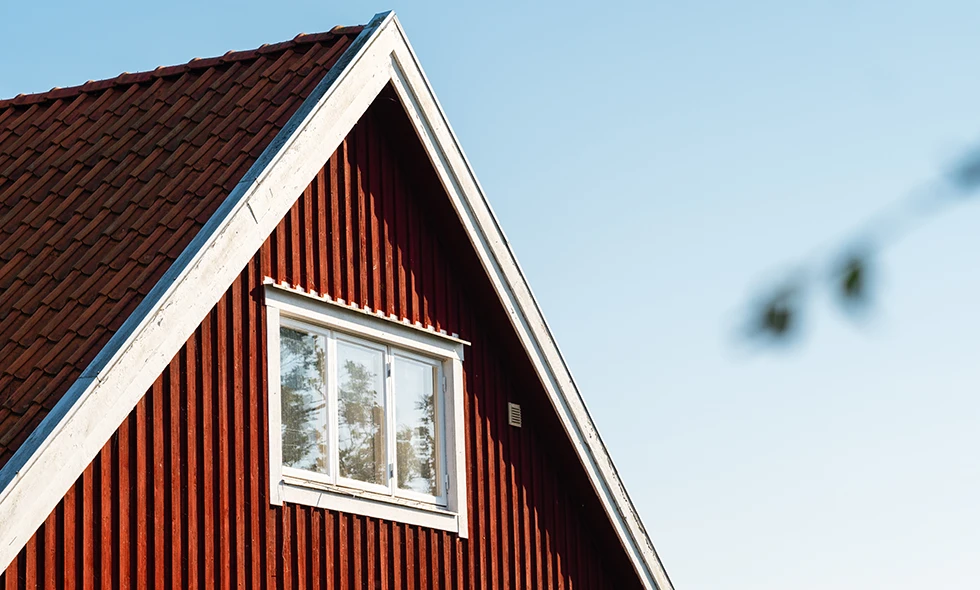 Gavel av ett rött trähus med vita knutar och tak med tegelpannor under klarblå himmel.