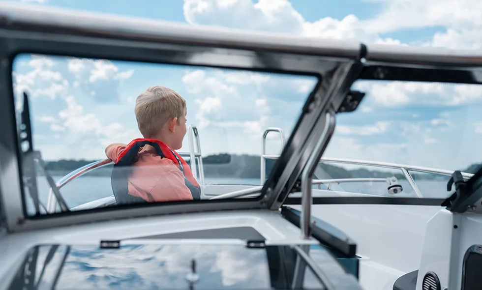 Pojke i rödorange flytväst sitter på en båt till sjöss och tittar ut över vattnet.