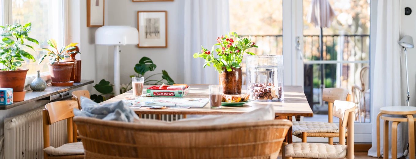 Ljus matplats med stolar, blombukett på bordet och stora glasdörrar som vetter mot en balkong.